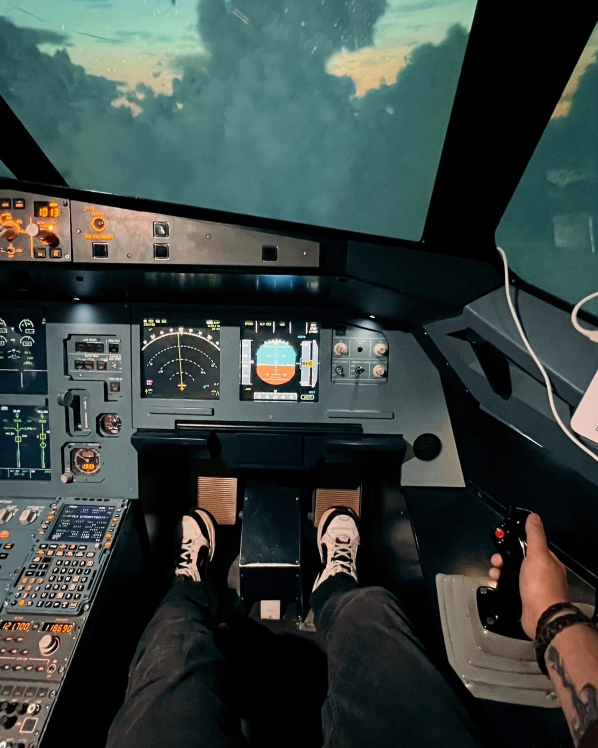 Вид с места пилота Airbus A320: ноги на педалях, рука на сайдстике, впереди облака