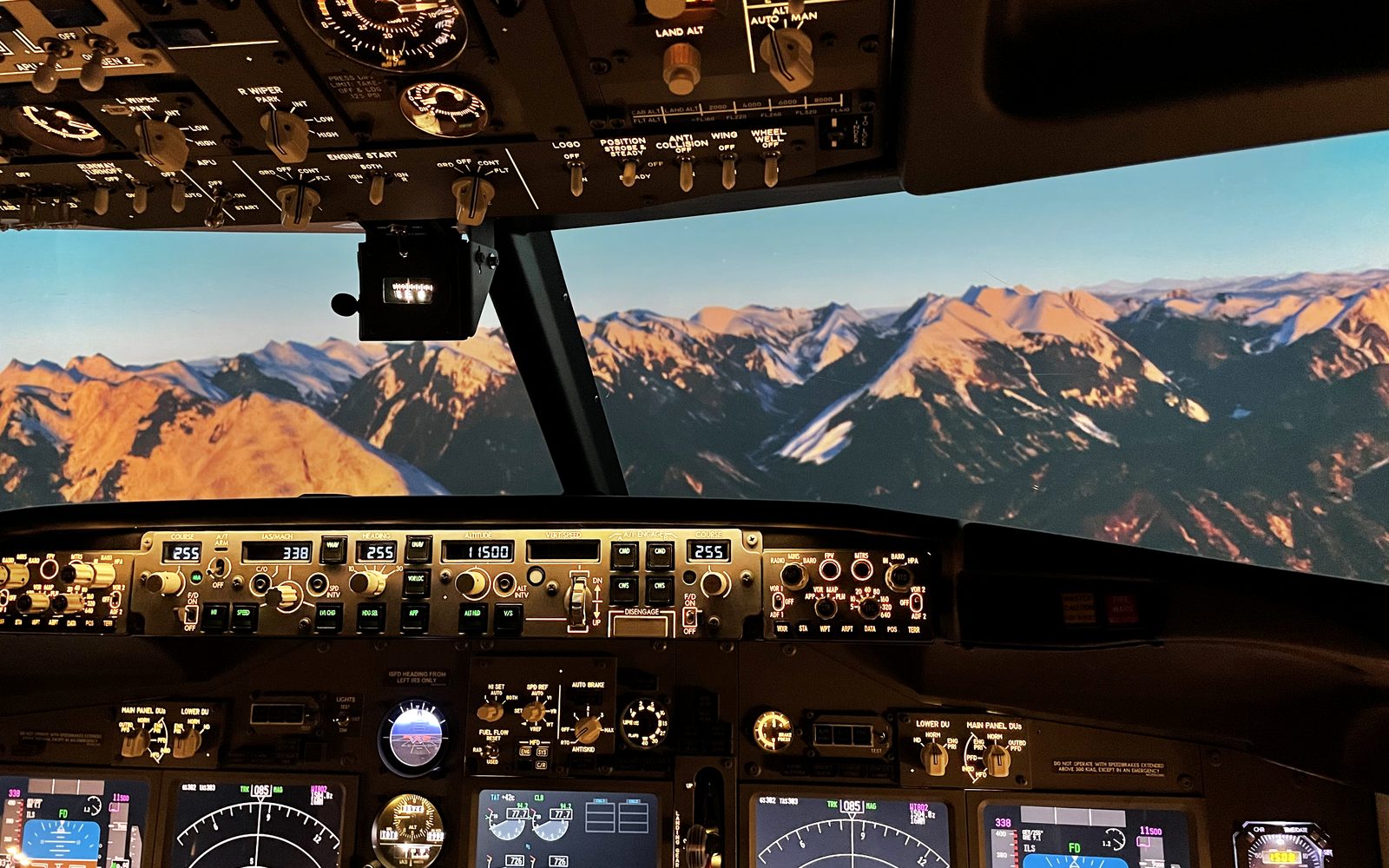 Кабина авиатренажёра Boeing 737 NG: горы на закате за остеклением, панель автопилота и приборы